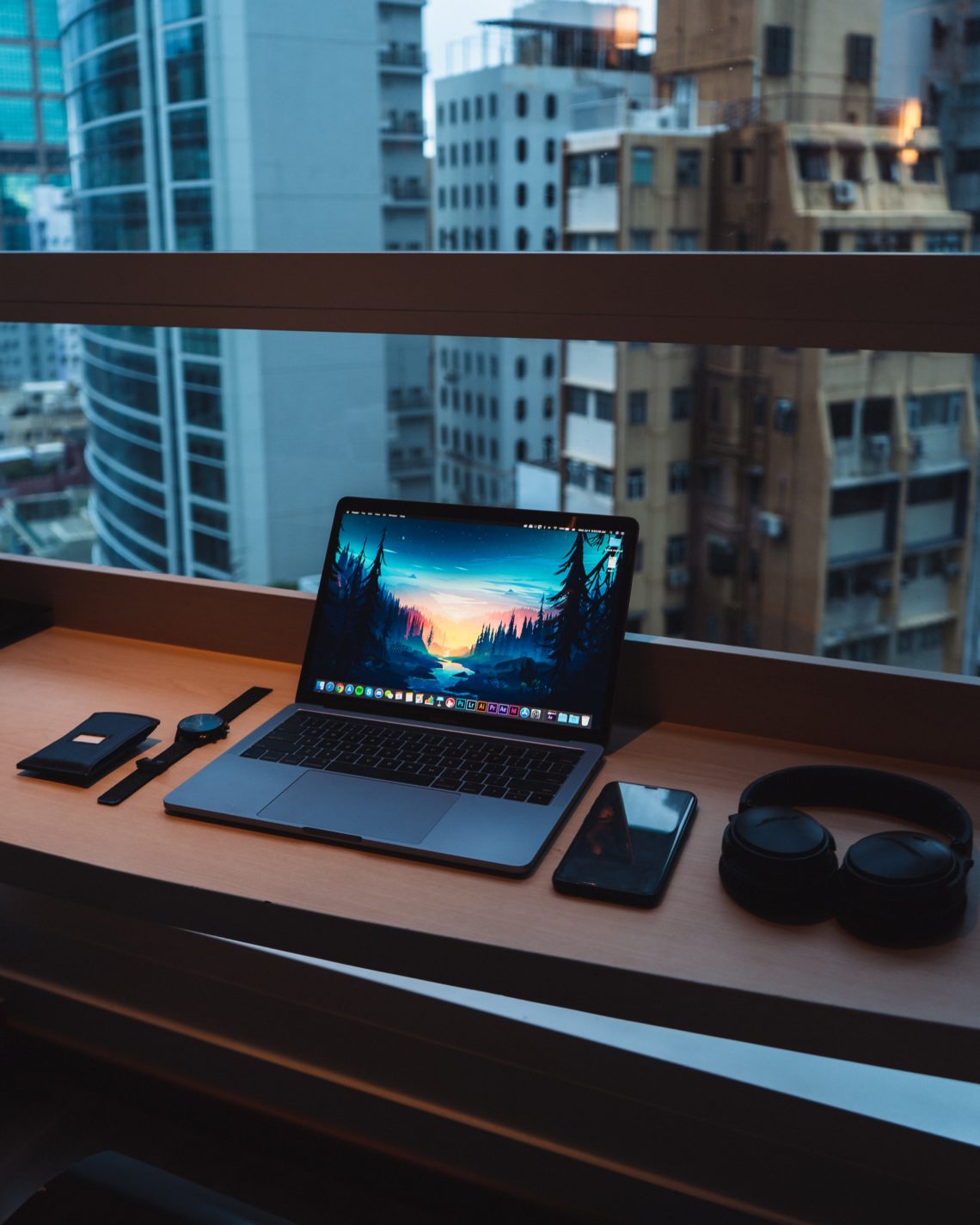 Photo of a computer, phone, headphones, and watch overlooking a city view.